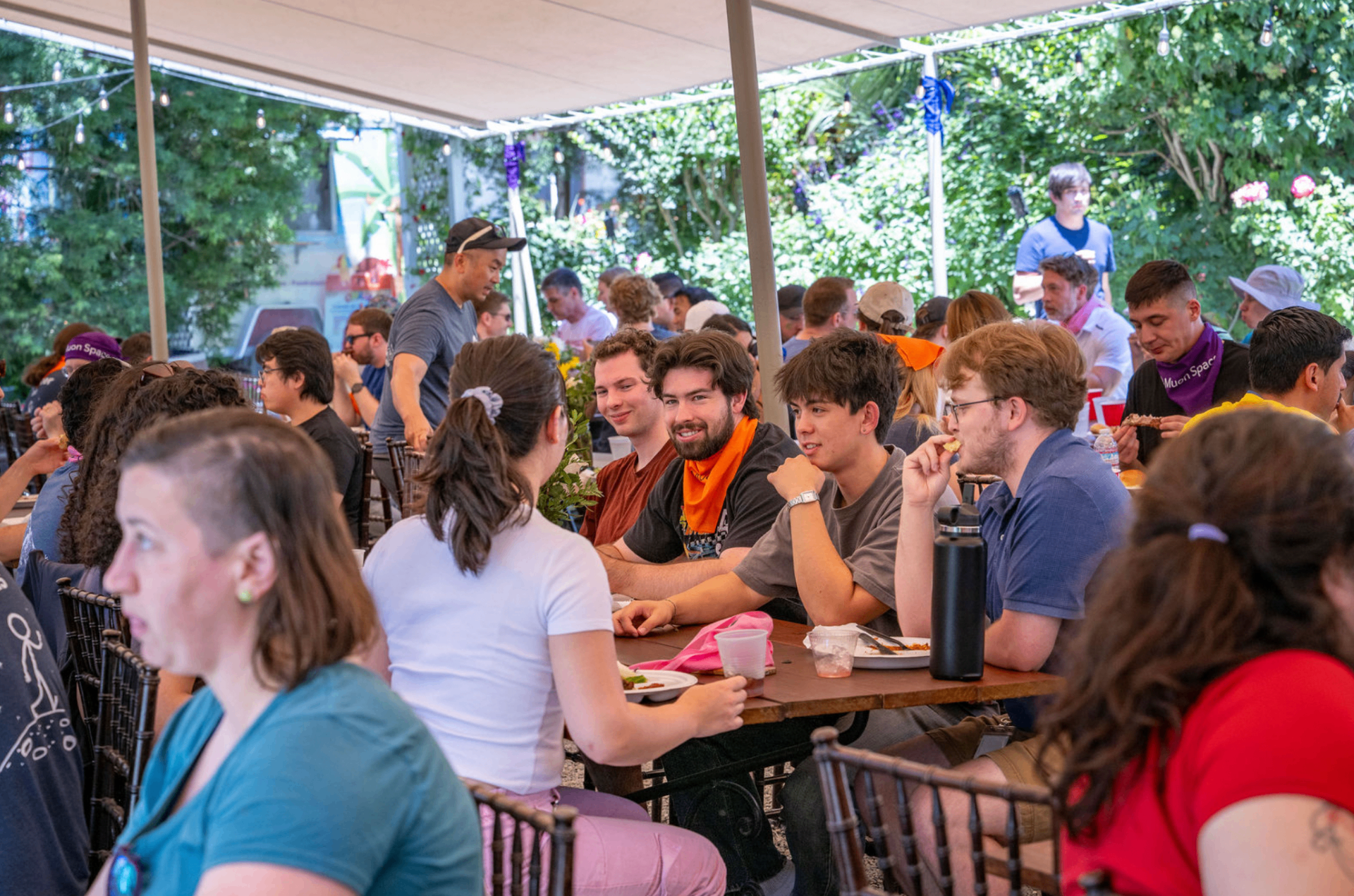 A packed outdoor lunch under string lights