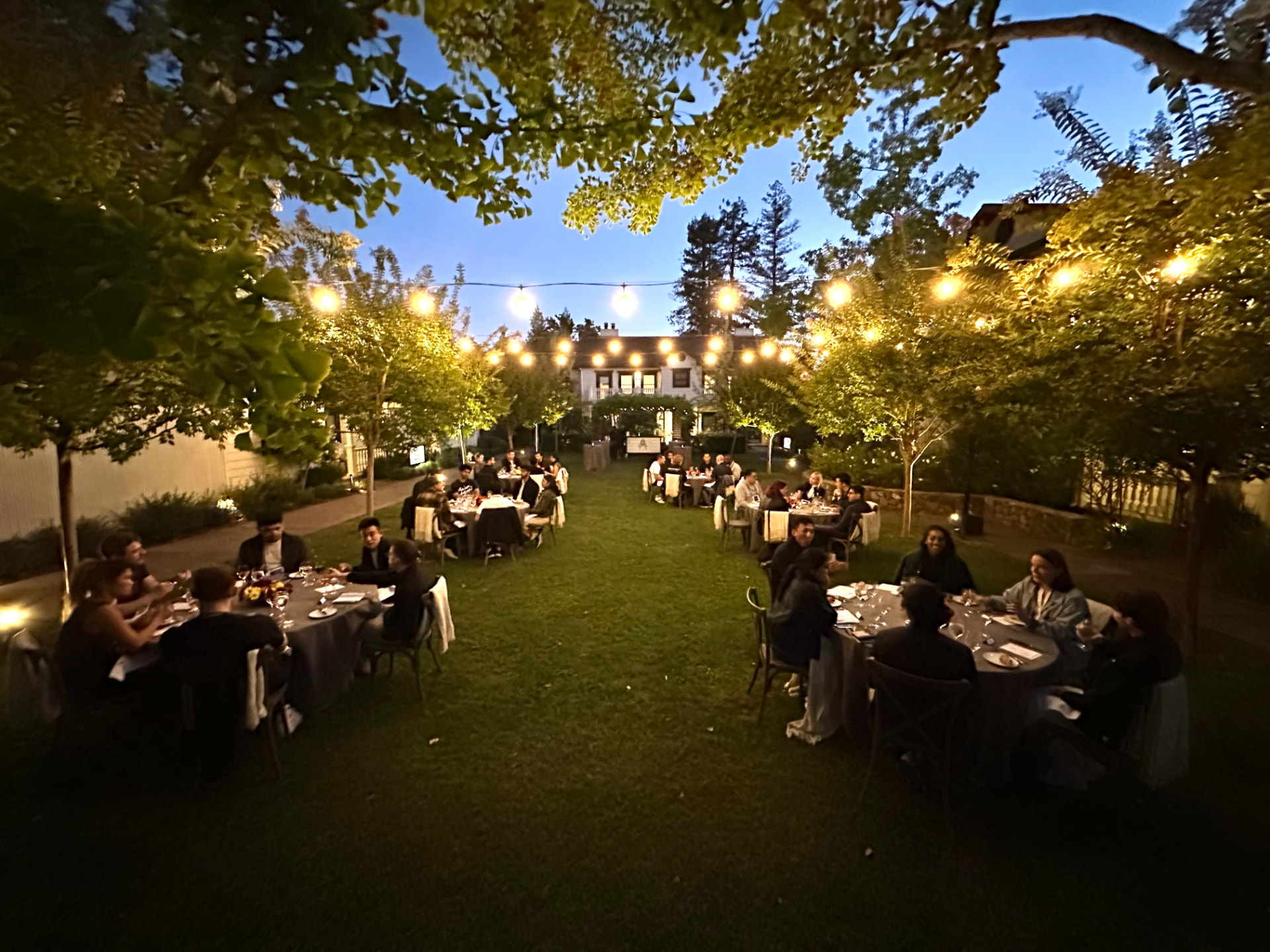 Outdoor dinner under string lights with guests at round tables